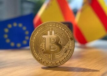 Una imagen con una moneda de bitcoin en primer plano y de fondo una bandera de España y la Unión Europea.